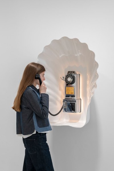 A woman picks up an old payphone housed in a large white case. 