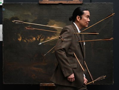 A man in a suit with an arrow in his body walks past a moody landscape painting.