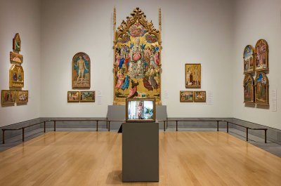 There is a gold-framed television on a pedestal in the museum gallery, which contains early Renaissance gold-leaf paintings. 