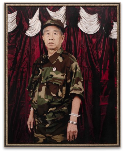 An old Miao man wearing camouflage military uniform poses for the camera.