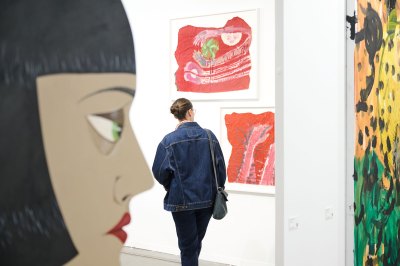 A woman looks at two prints at an art fair booth, with other works visible in the foreground. 