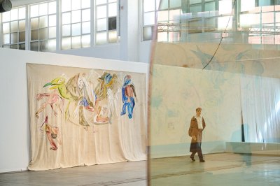 A man walks through an art fair and is seen through a transparent fabric. 