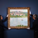 Two art conservators hold a colorful landscape painting by French Impressionist painter Claude Monet against a dark wall