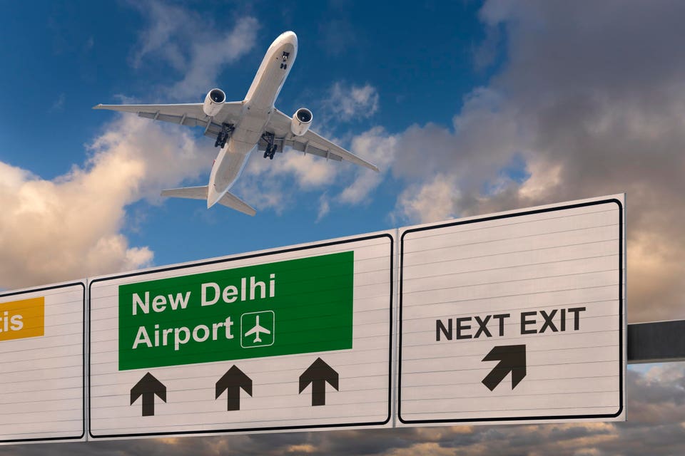 Road signs indicating the direction to New Delhi Airport and a plane that has just taken off.