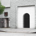 View of a gray building with a mural on the garage at the arched entrance. A neon sign reads 