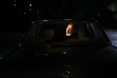A person stares out from the back of a car, they are dramatically lit at night.