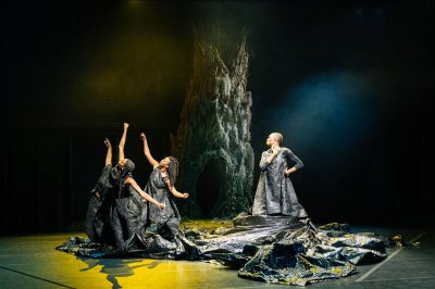 three performers on stage in front of what looks like a tree with dramatic lighting.