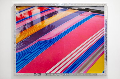 A detailed close-up of a pink lowrider's hood with palm trees reflected. It is framed in a metal engraved frame. 
