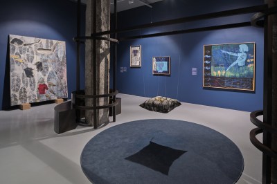 The gallery is hung with textiles and a large blue rug.