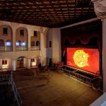 A photo shows a large dark theater with a movie screen showing an image of a burning star