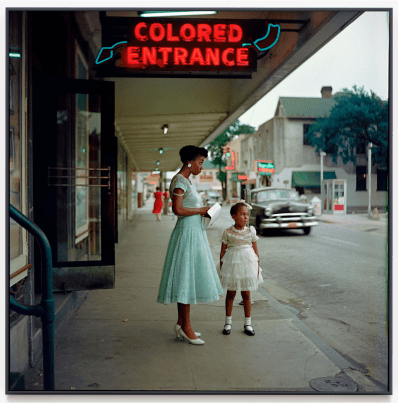 A black mother and daughter, dressed in their Sunday best, stood outside a department store with a neon sign that read 