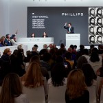 Phillips Auction House was auctioning Lot 15 (an Andy Warhol work) live, and the place was packed with people. The auctioneer stands on a podium with one arm raised, with a telephone bidder on his left. The price board displays data for multiple currencies (USD, EUR, GBP, CHF, HKD), and the screen to the right displays a portrait of Warhol—a grid of repeating portrait images in his signature style. Spectators sat in rows of white chairs, mostly watching from behind.